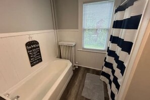 A bathroom with a white bathtub, a window with blinds, a radiator, and a striped shower curtain.