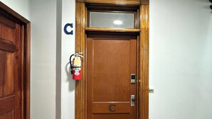 Uma porta de madeira com puxador de metal e alarme de incêndio na parede.