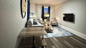 Uma sala de estar com uma mesa de madeira, dois sofás, uma TV e uma janela com cortinas.