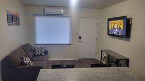 A living room with a gray couch, a white door, and a TV mounted on the wall displaying 'Animal Control'.