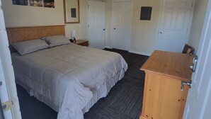 A bedroom with a large bed, a wooden dresser, a nightstand, a mirror, and two doors.