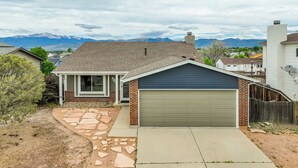 Une maison d’habitation avec un garage, un chemin en pierre et une vue sur les montagnes en arrière-plan.