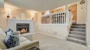 Un salon avec une cheminée, un escalier et des meubles de rangement en bois.