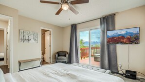 Une chambre avec un grand lit, un ventilateur de plafond, une télévision et une vue sur une terrasse et les montagnes.