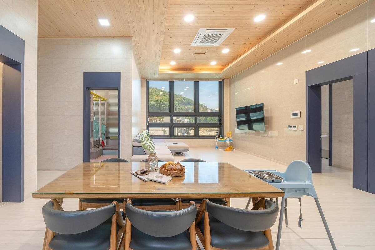 A modern dining area with a wooden table, four chairs, a vase, and a basket of bread.