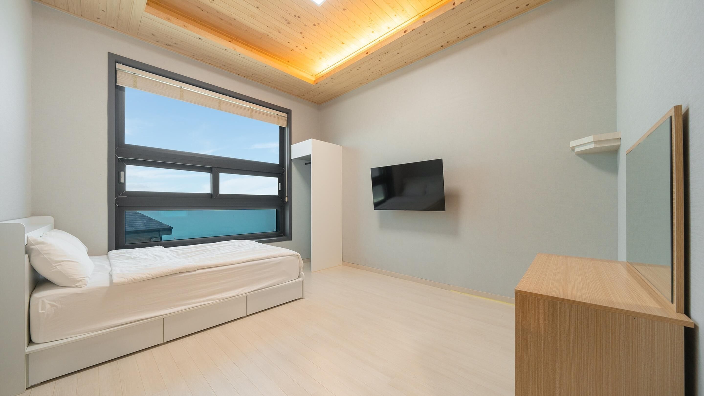 Ein modernes Schlafzimmer mit einem Bett, einem Fernseher, einem großen Fenster und einer Holzbalkendecke.