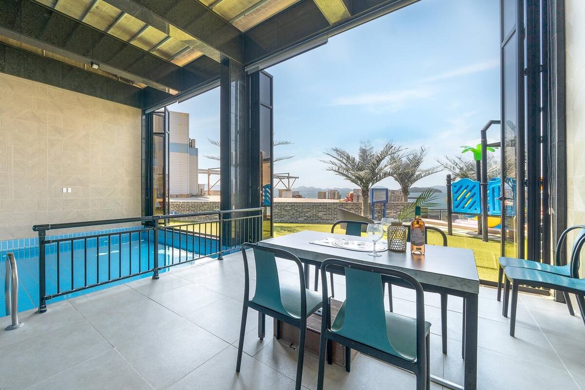 A modern outdoor dining area with a pool, large windows, and a view of the cityscape.