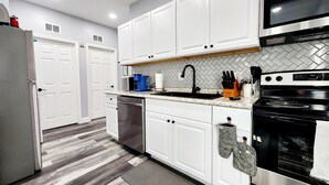Een moderne keuken met witte kastjes, roestvrijstalen apparatuur, een zwarte kraan en een betegelde achterwand.