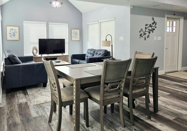 A modern living room with a flat-screen TV, a sofa, a dining table with chairs, and a decorative wall piece.