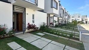 Un edificio residencial moderno con techo plano, amplias ventanas y un césped cuidado con senderos de piedra.