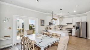 Une cuisine moderne avec des meubles blancs, un réfrigérateur en acier inoxydable et un coin repas comprenant une table blanche et des chaises en bois.