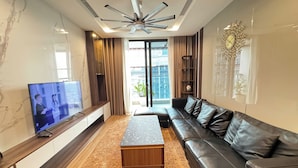 A modern living room with a flat-screen TV, a leather sofa, a wooden coffee table, and a ceiling fan. - Royal Condotel in Vinhomes Metropolis (Hanoi)
