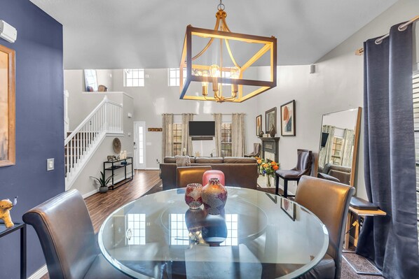 A modern living room with a glass table, leather chairs, a brown sofa, and a chandelier.
