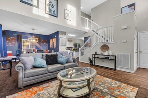 A spacious living room with a grey sofa, a glass coffee table, and a staircase leading to an upper level.