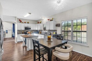 A modern kitchen with white cabinetry, a central island, and a dining area with a table and chairs.
