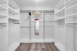 Un dressing avec des étagères blanches, une tringle à vêtements et une porte dotée d’un paillasson à motifs.