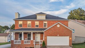 A two-story brick house with a front porch, a garage, and a well-maintained lawn.