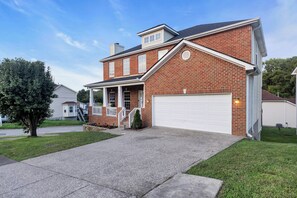 A two-story brick house with a front porch, a garage, and a well-maintained lawn.