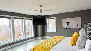 Une chambre avec un grand lit, un ventilateur de plafond et un tableau accroché au mur.