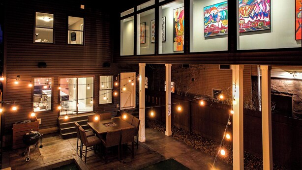 Une maison dotée d’un patio aménagé avec une table et des chaises, des guirlandes lumineuses et des œuvres d’art accrochées aux murs.