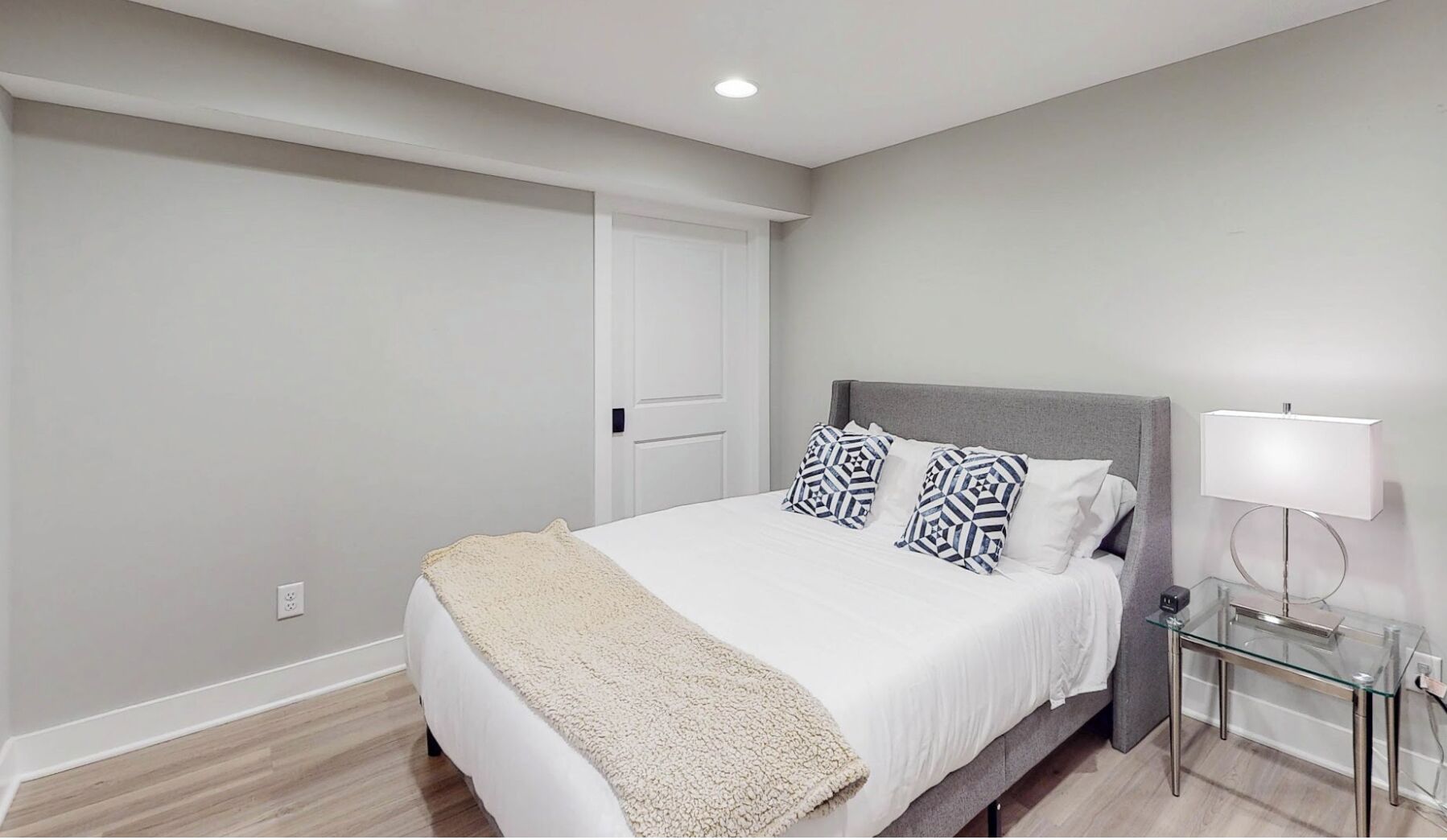 Une chambre à coucher moderne avec un lit, une table de chevet avec une lampe et une porte.