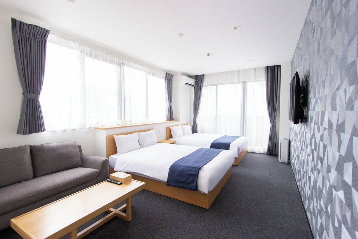 A hotel room with two beds, a sofa, a small table, and a TV mounted on the wall.