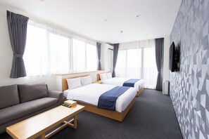 Ein Hotelzimmer mit zwei Betten, einem Sofa, einem kleinen Tisch und einem an der Wand montierten Fernseher.