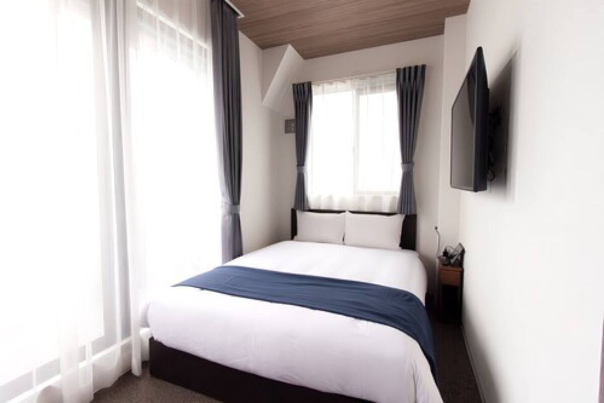 A hotel room with a large bed, a flat-screen TV mounted on the wall, and a window with curtains.