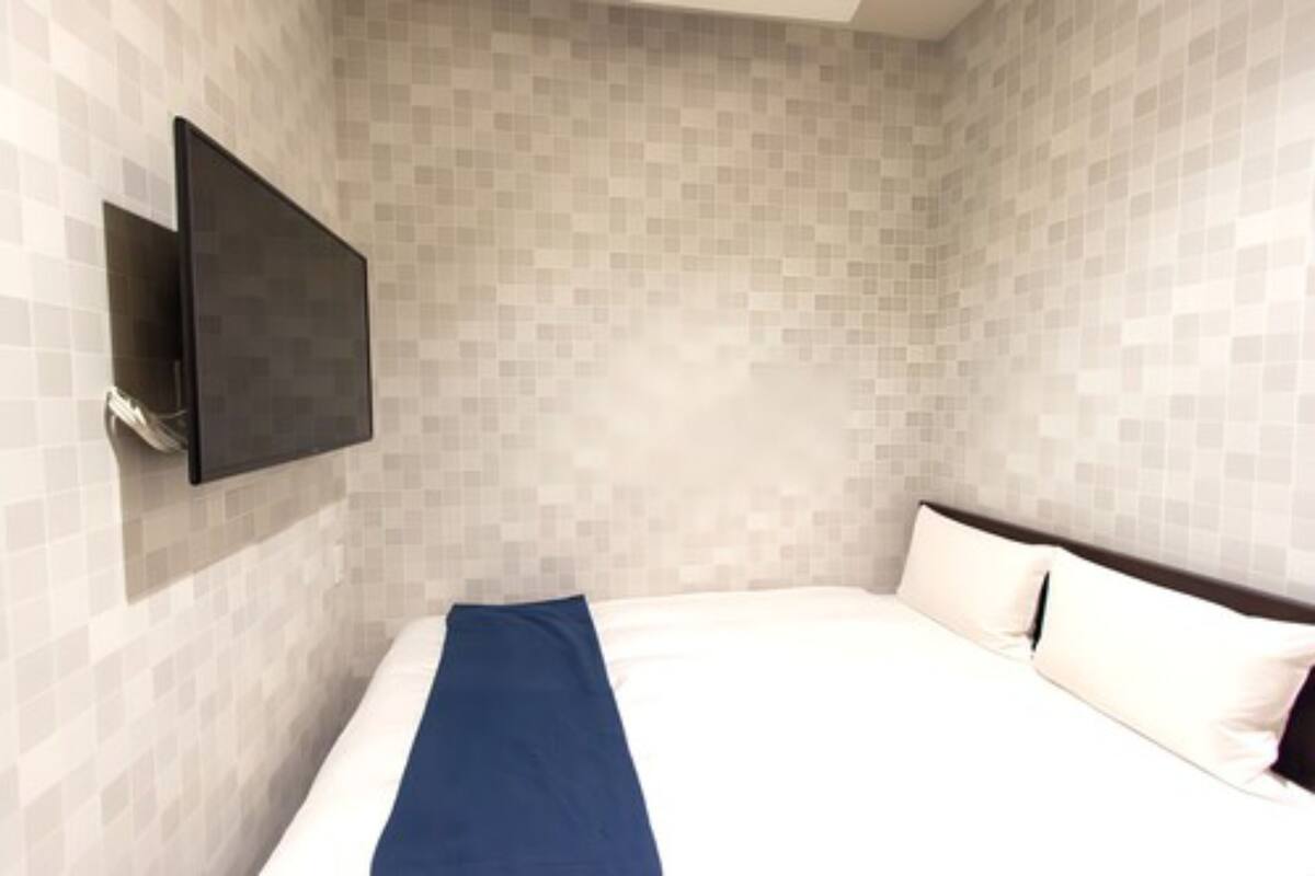 A hotel room with a bed, a flat-screen TV mounted on the wall, and a tiled wall.