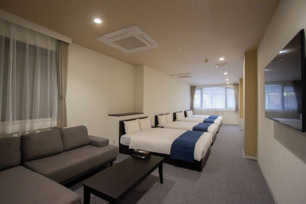 A hotel room with a sofa, two beds, a TV, and a large window.