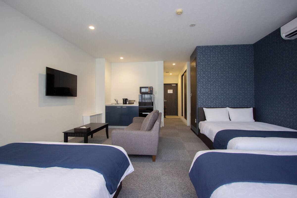 A hotel room with two beds, a sofa, a TV, and a kitchenette.
