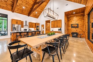 A modern kitchen with wooden cabinets, stainless steel appliances, and a large dining table with chairs. - Spacious Luxe 4BR | Game Room | Fire Pit & Hot Tub (Broken Bow)