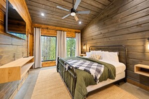 A wooden cabin bedroom with a bed, a ceiling fan, a window with curtains, and a shelf. - Spacious Luxe 4BR | Game Room | Fire Pit & Hot Tub (Broken Bow)