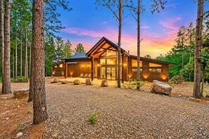 Une cabane en rondins moderne, dotée d’une grande entrée vitrée, entourée d’une allée en gravier et de gros rochers.