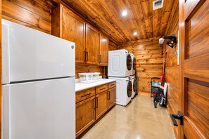 A compact kitchen with wooden cabinets, a white refrigerator, a stacked washer and dryer, and a ceiling-mounted projector.