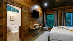 Une chambre dans une cabane en bois, avec un grand lit, un téléviseur fixé au mur et une fenêtre avec des rideaux.