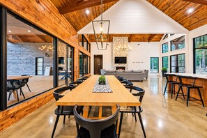 Un vaste espace dédié à la salle à manger, avec une longue table en bois, des chaises noires et une plante placée au centre.