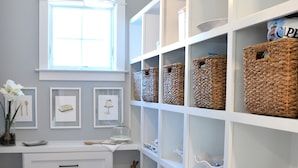 Un espace de rangement bien organisé, avec des étagères blanches, des paniers en osier et un tapis à carreaux bleus.