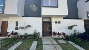 A modern two-story house with a central entrance, a small garden with various plants, and a clear sky. - Puerto Vallarta Altavela Egina 62 (Valle de Banderas)