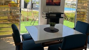 A dining area with a table and chairs, a painting of a sunset, and a view of a pool and garden. - Puerto Vallarta Altavela Egina 62 (Valle de Banderas)