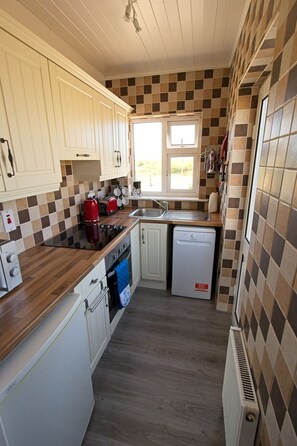 A compact kitchen with white cabinets, a wooden countertop, a built-in oven, a dishwasher, and a window providing natural light.