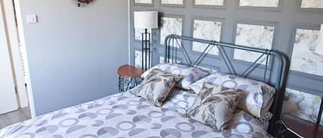 A bedroom with a bed, a chair, a lamp, and a wall-mounted guitar decoration.