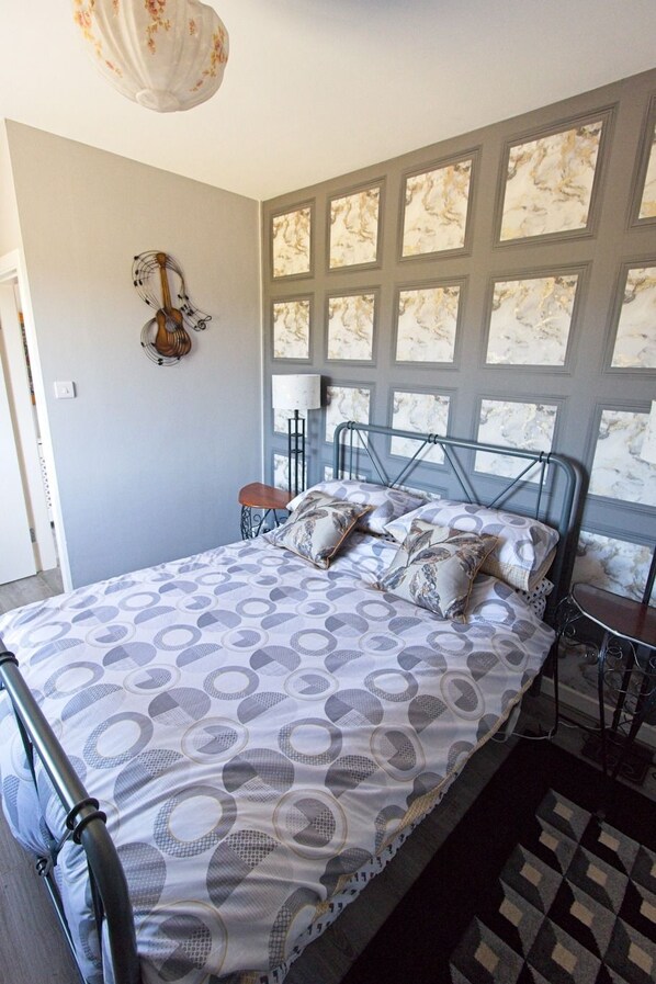 A bedroom with a bed, a chair, a lamp, and a wall-mounted guitar decoration.