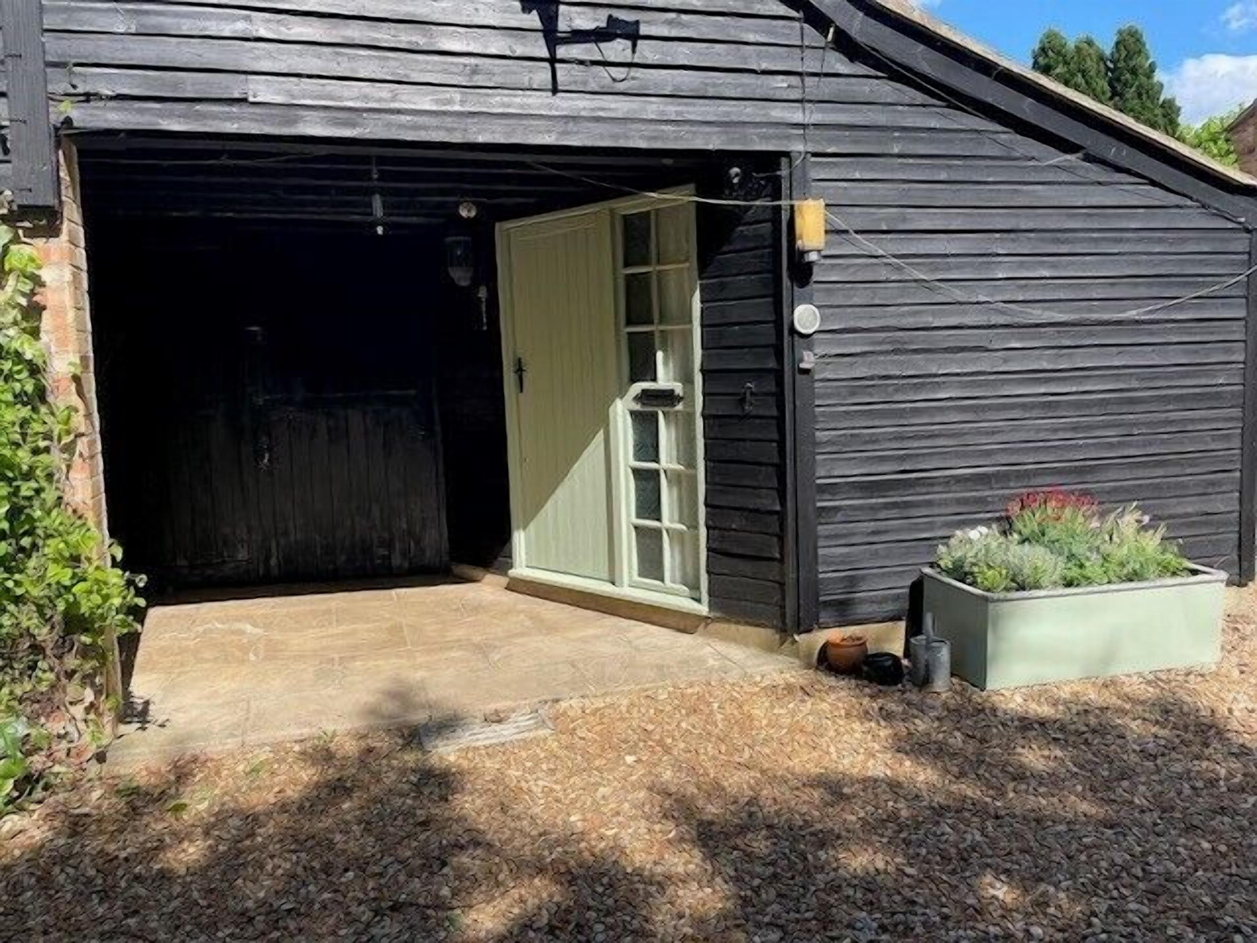 Eine Garage mit einer weißen Tür, einem kleinen Podest davor und einem Blumenkasten mit Pflanzen auf der rechten Seite.