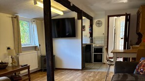 Un salon spacieux avec un plancher en bois, un canapé, un téléviseur et un coin cuisine à l’arrière-plan.