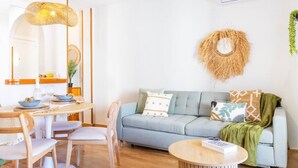 Een moderne woonkamer met een lichtblauwe bank, een ronde houten salontafel en een eethoek met een houten tafel en stoelen.