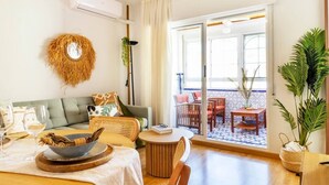 Een gezellige woonkamer met een bank, een ronde houten tafel en een balkon met tuinmeubilair.