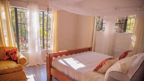 Une chambre à coucher avec un lit en bois, un fauteuil jaune et une grande fenêtre avec des rideaux.