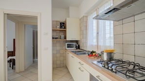 Een moderne keuken met een gasfornuis, magnetron en een spoelbak. Er zijn kastjes en een aanrecht met groenten en een pan.