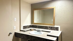 A bathroom with a white sink, black marble countertop, and a mirror with a wooden frame. - Regency Inn Fresno (Fresno)